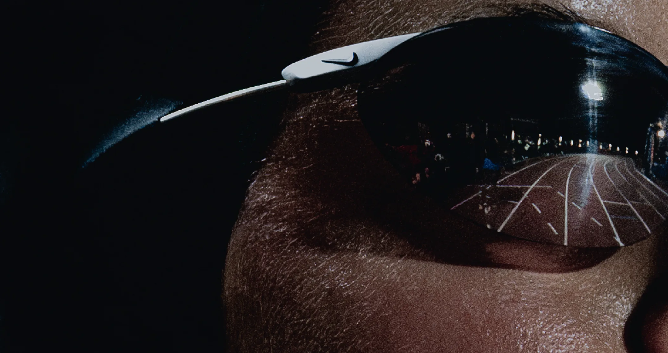 Close-up of an athlete's eye behind wraparound sunglasses, the track reflected in the lens