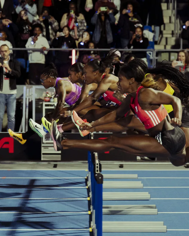 Hurdlers clearing a barrier in front of a packed crowd