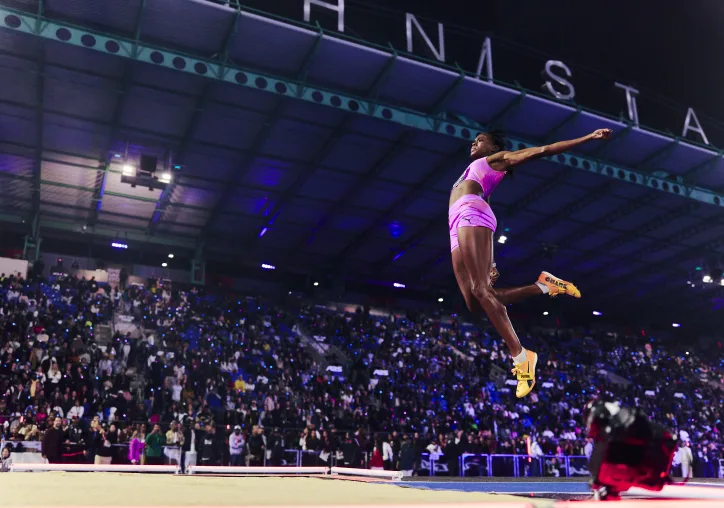 A long jumper in mid-flight in front of the full stadium at night