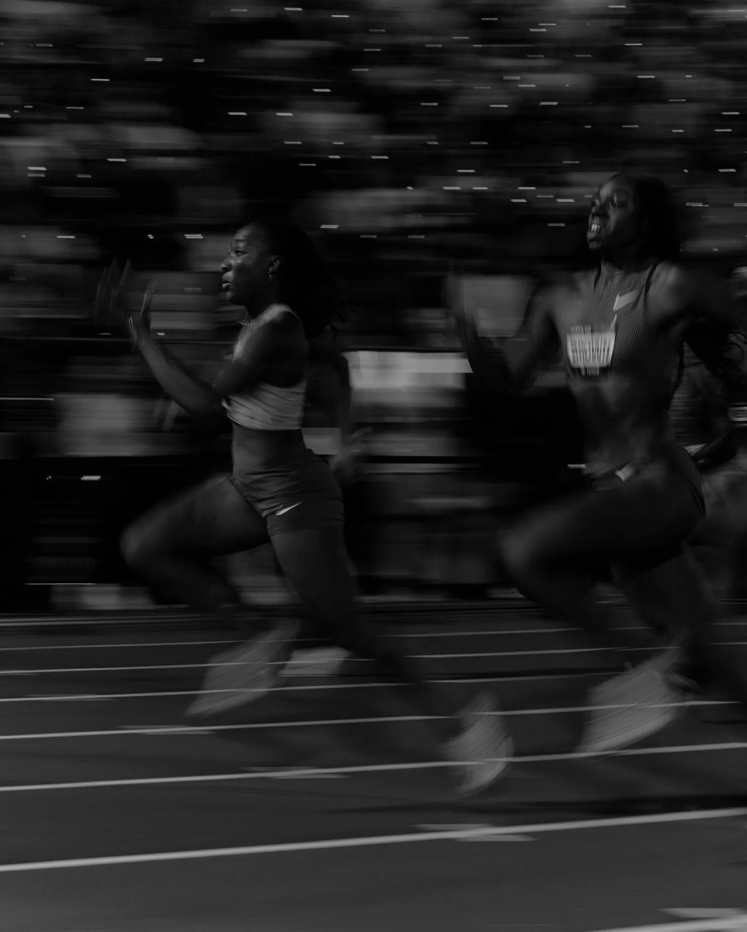 Sprinters racing down the track at ATHLOS NYC, motion-blurred in black and white
